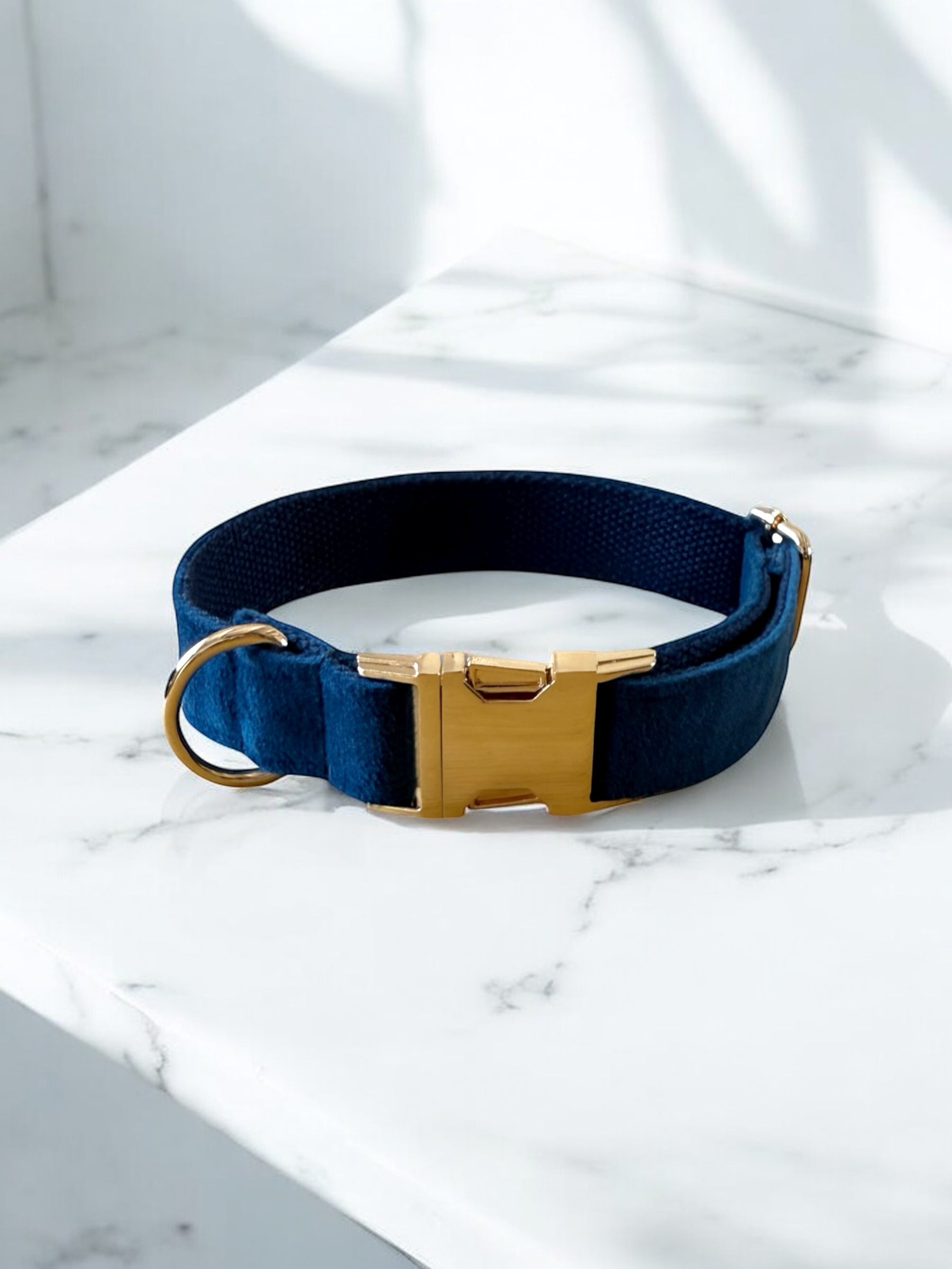 Navy blue dog collar with a gold buckle on a marble surface
