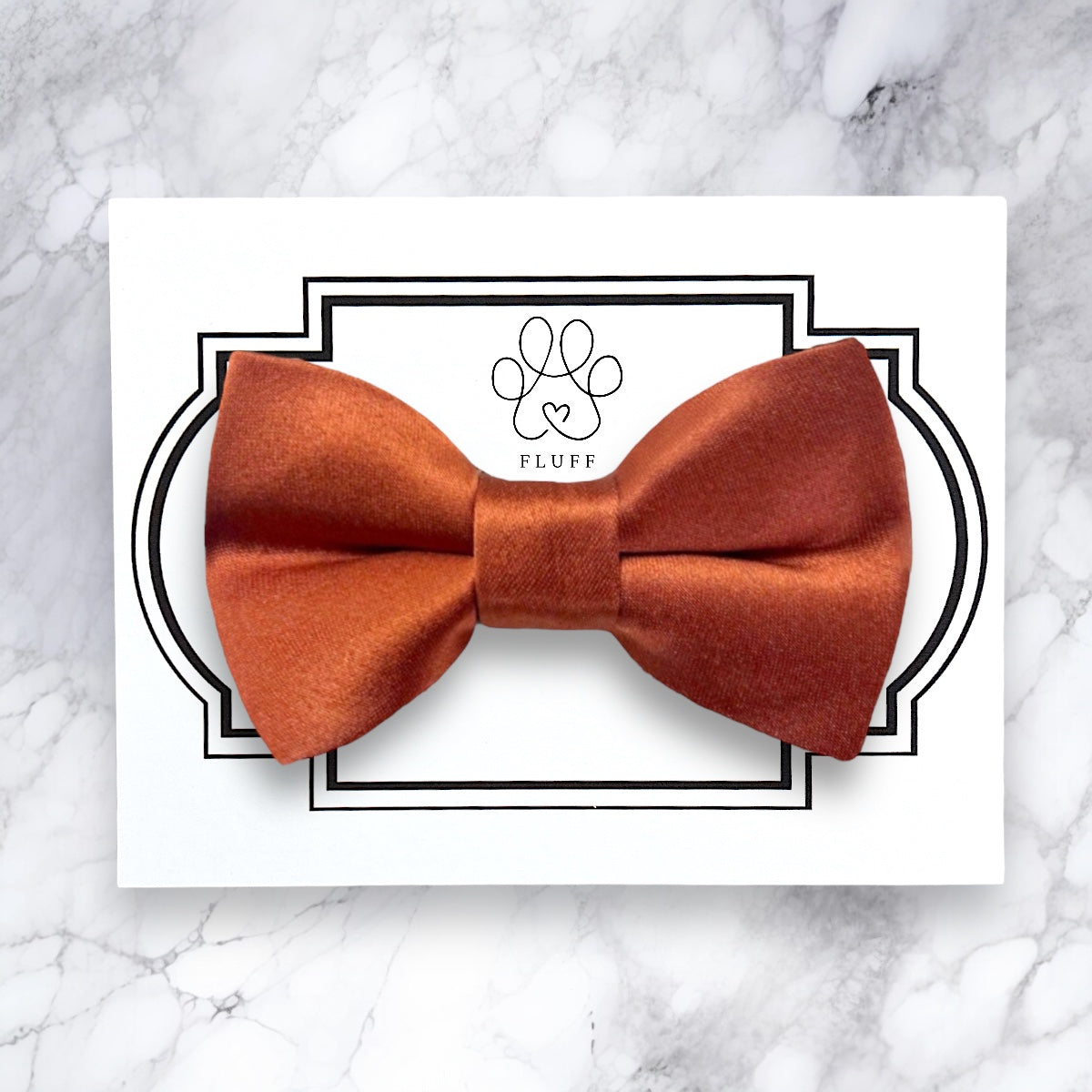 Terracotta dog bow tie on a white card with 'Fluff' branding on a marble background