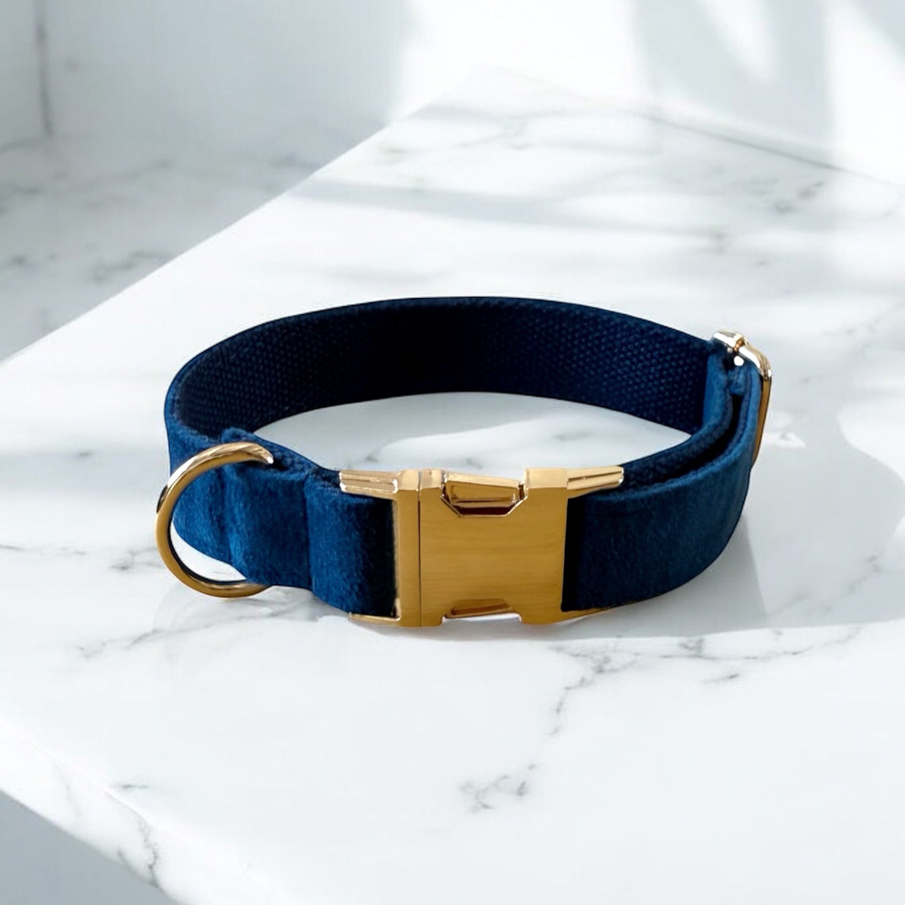 Navy blue dog collar with a gold buckle on a marble surface