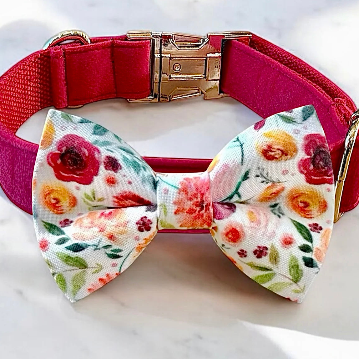 A pink collar with a floral print bow tie is displayed on a white marble surface.