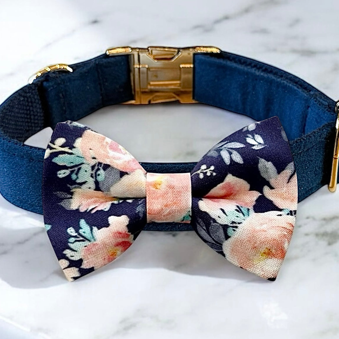 A navy blue dog collar with a gold buckle and a bow tie with a floral pattern.