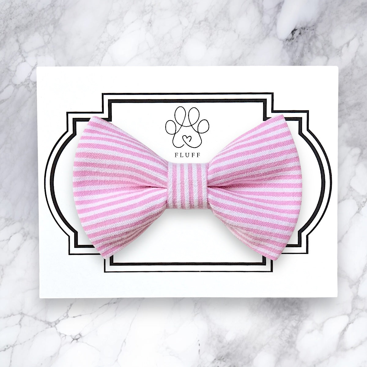Pink striped bow tie on a white card with 'Fluff' brand logo on a marble background