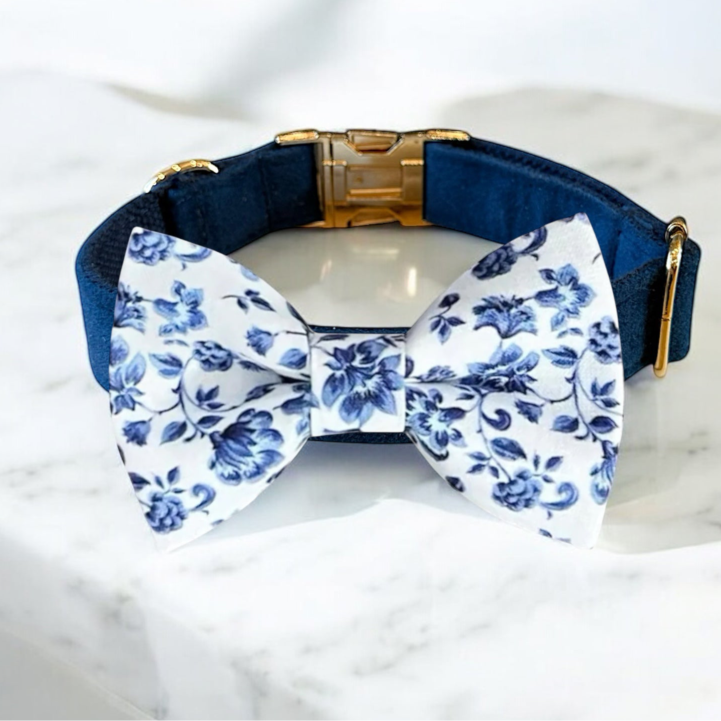 Navy dog collar with a white floral bow tie on a marble surface