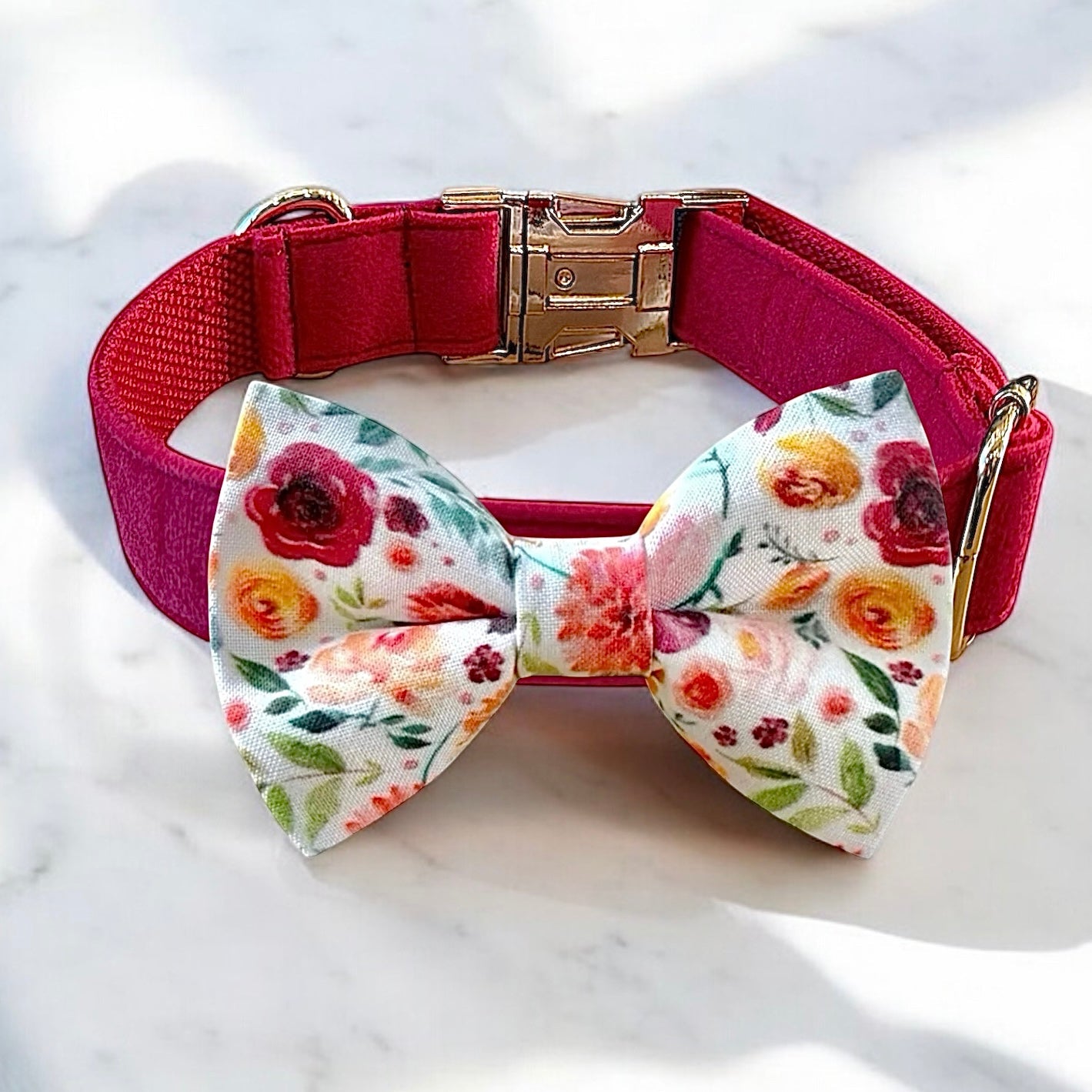 Floral bow tie on a pink collar with gold buckle on a white marble background