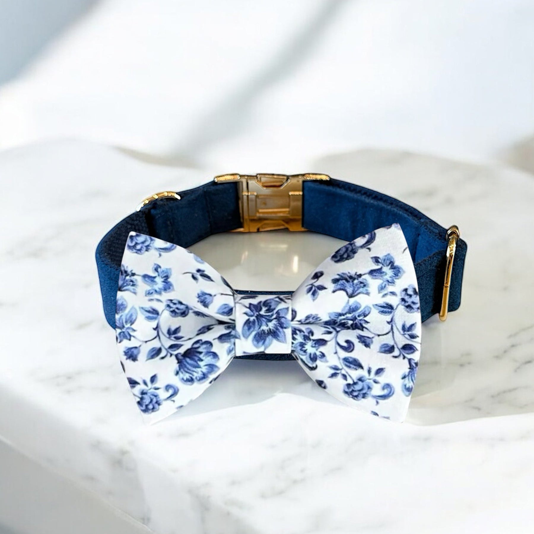 Navy blue dog collar with a white floral bow tie on a marble surface