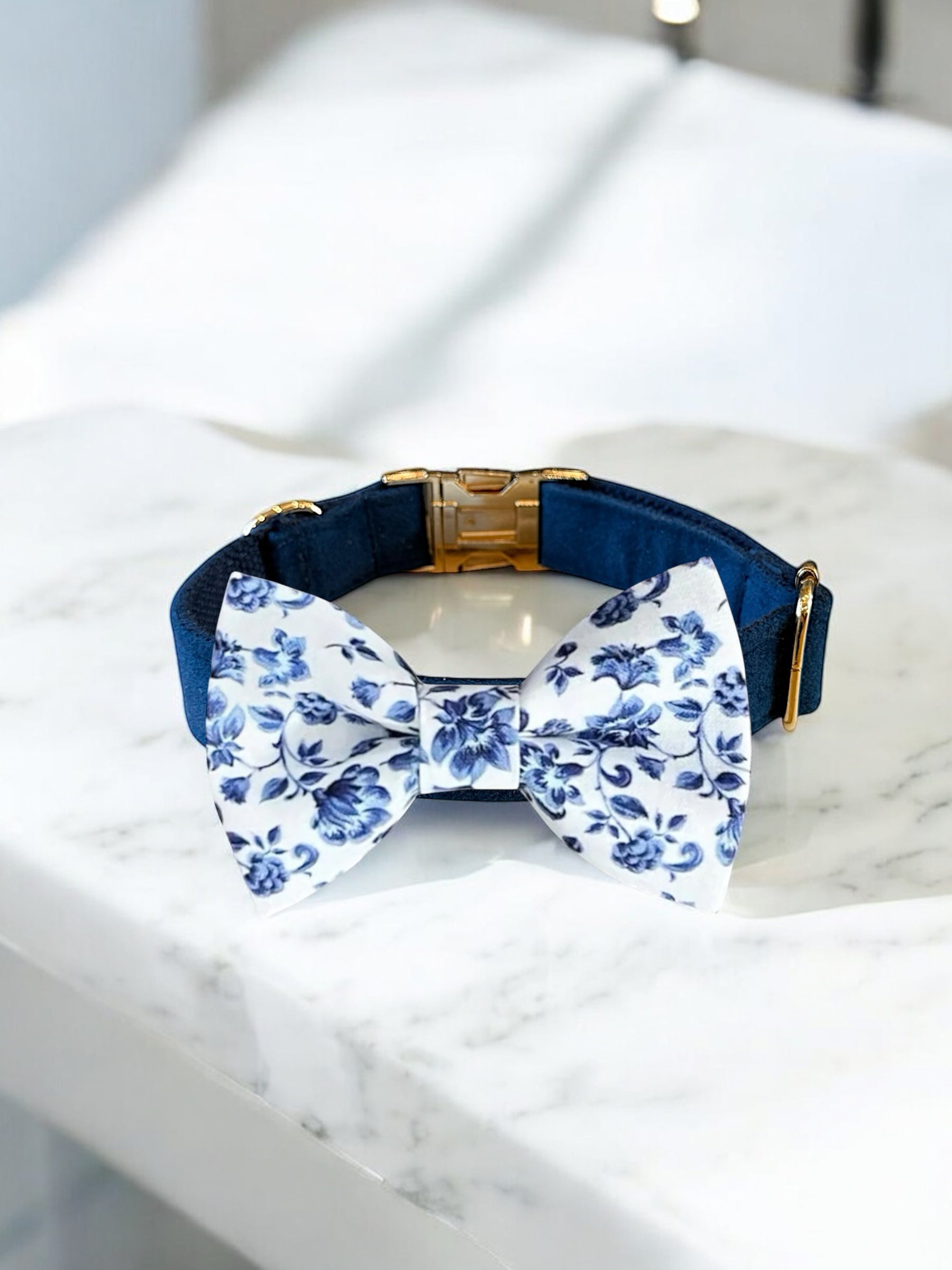 Navy blue dog collar with a white floral bow tie on a marble surface