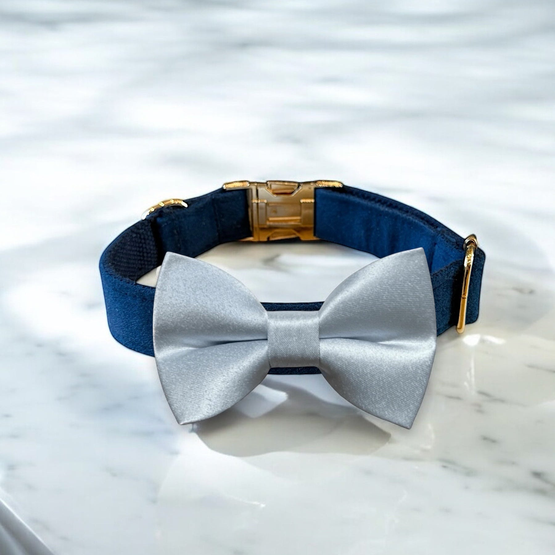 Navy blue dog collar with a gold clasp and blue bow tie on a marble surface