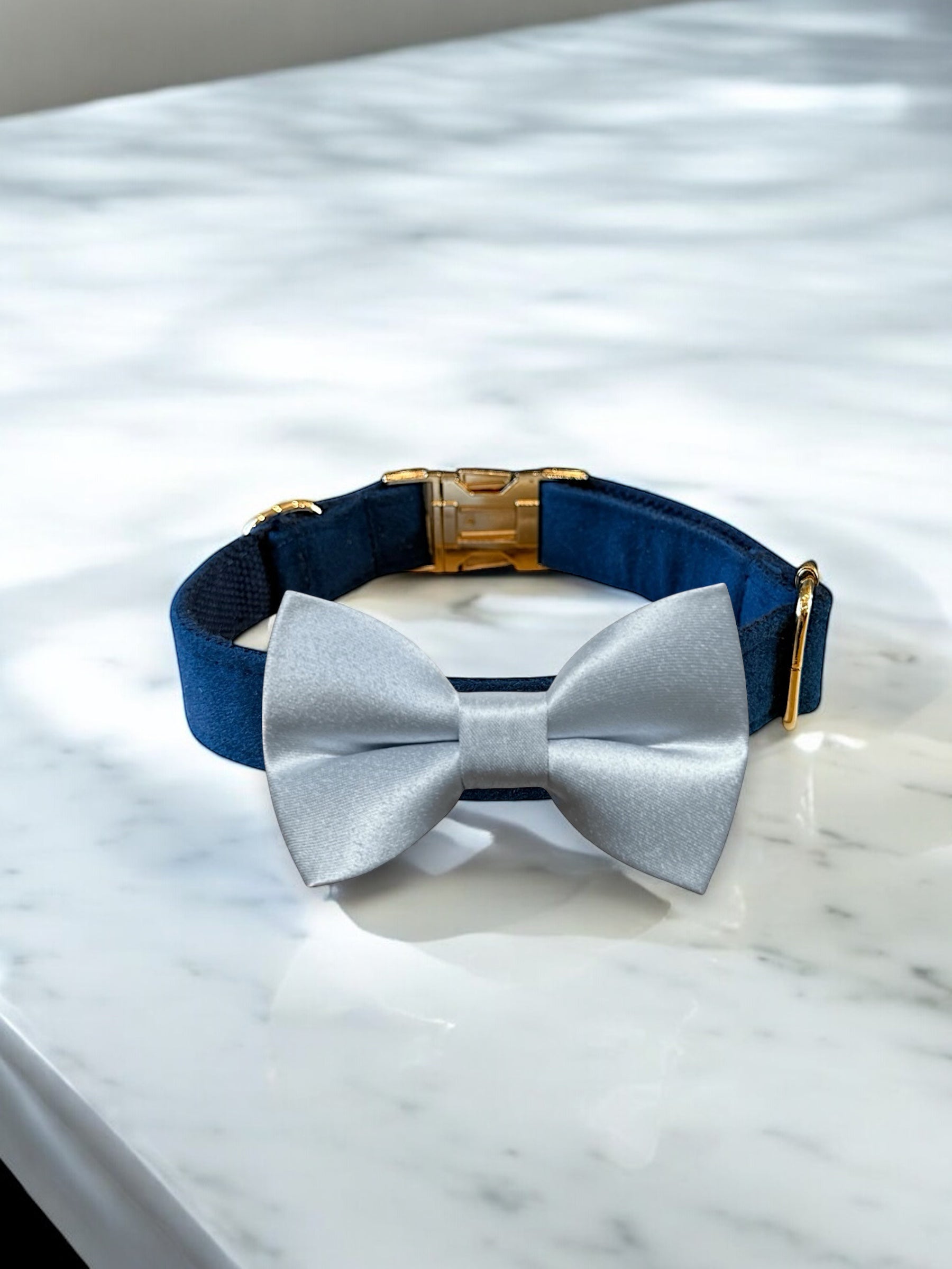 Navy blue dog collar with a gold clasp and blue bow tie on a marble surface