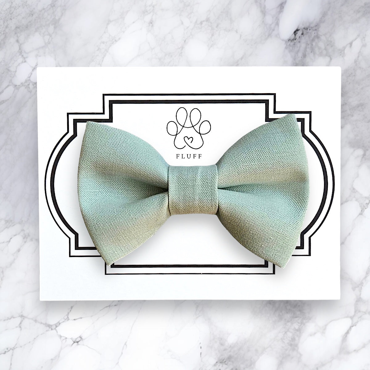 Green sage dog bow tie on a white card with 'Fluff' branding on a marble background