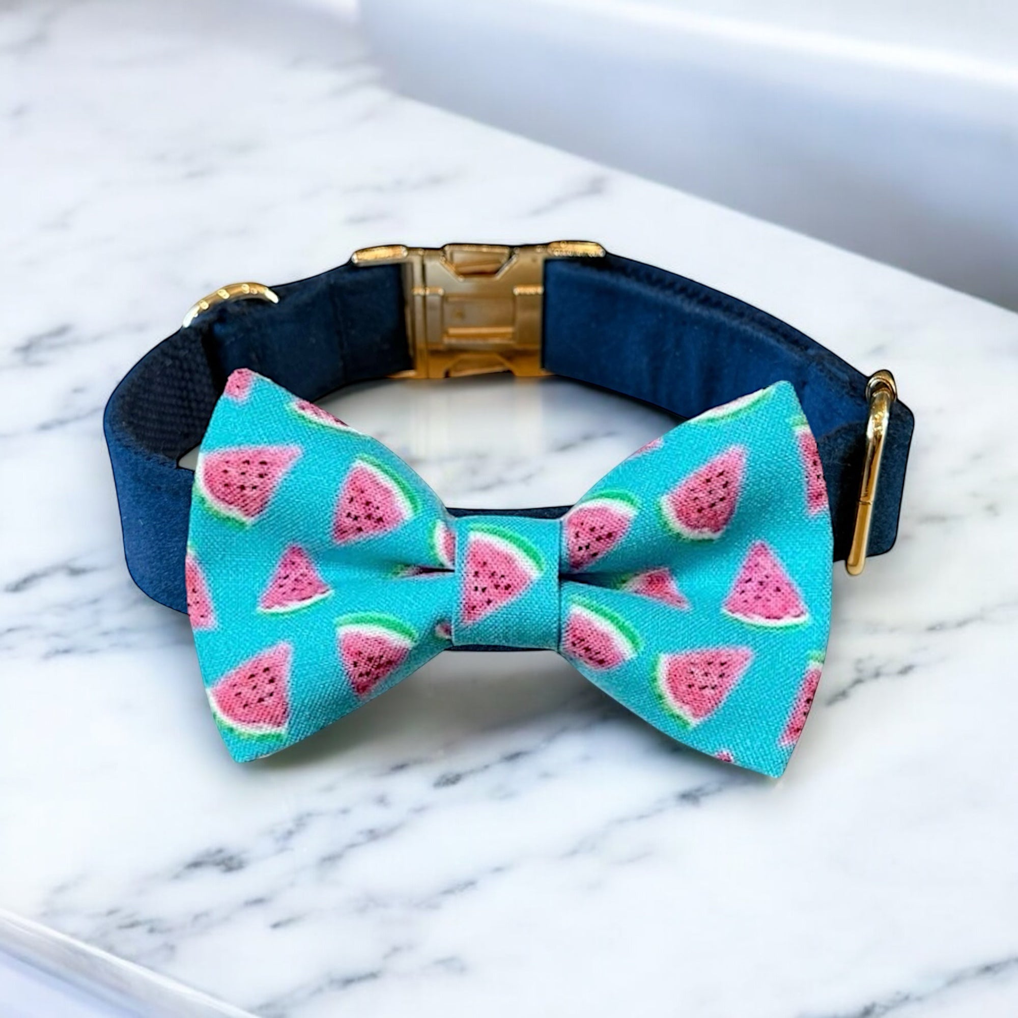 Navy blue dog collar with a watermelon patterned bow tie on a marble surface