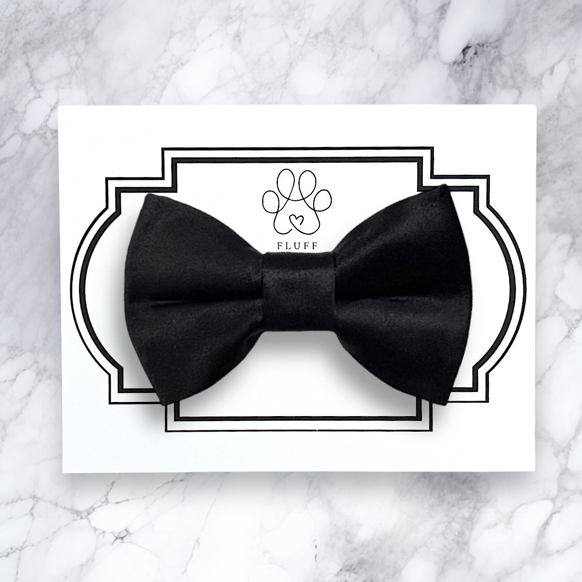Black dog bow tie on a white card with 'Fluff' brand logo on a marble background