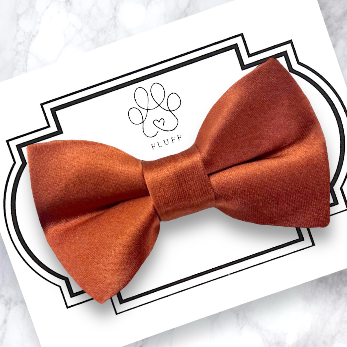 Orange dog bow tie on a white card with 'Fluff' branding, on a marble surface.