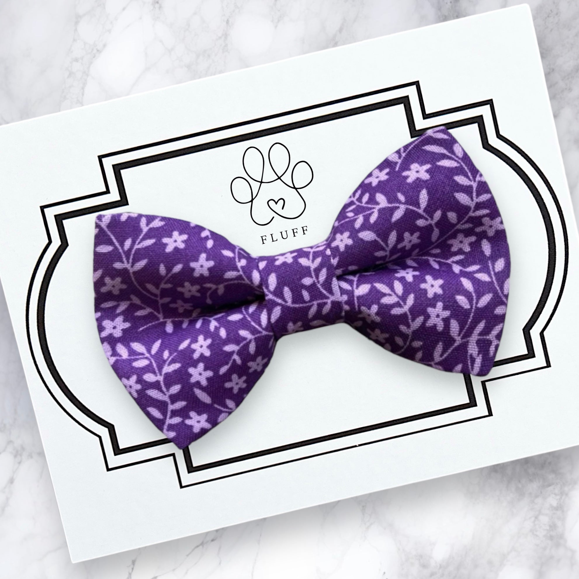 A dark purple floral bow tie for dogs or cats displayed on a white card with a black decorative border.