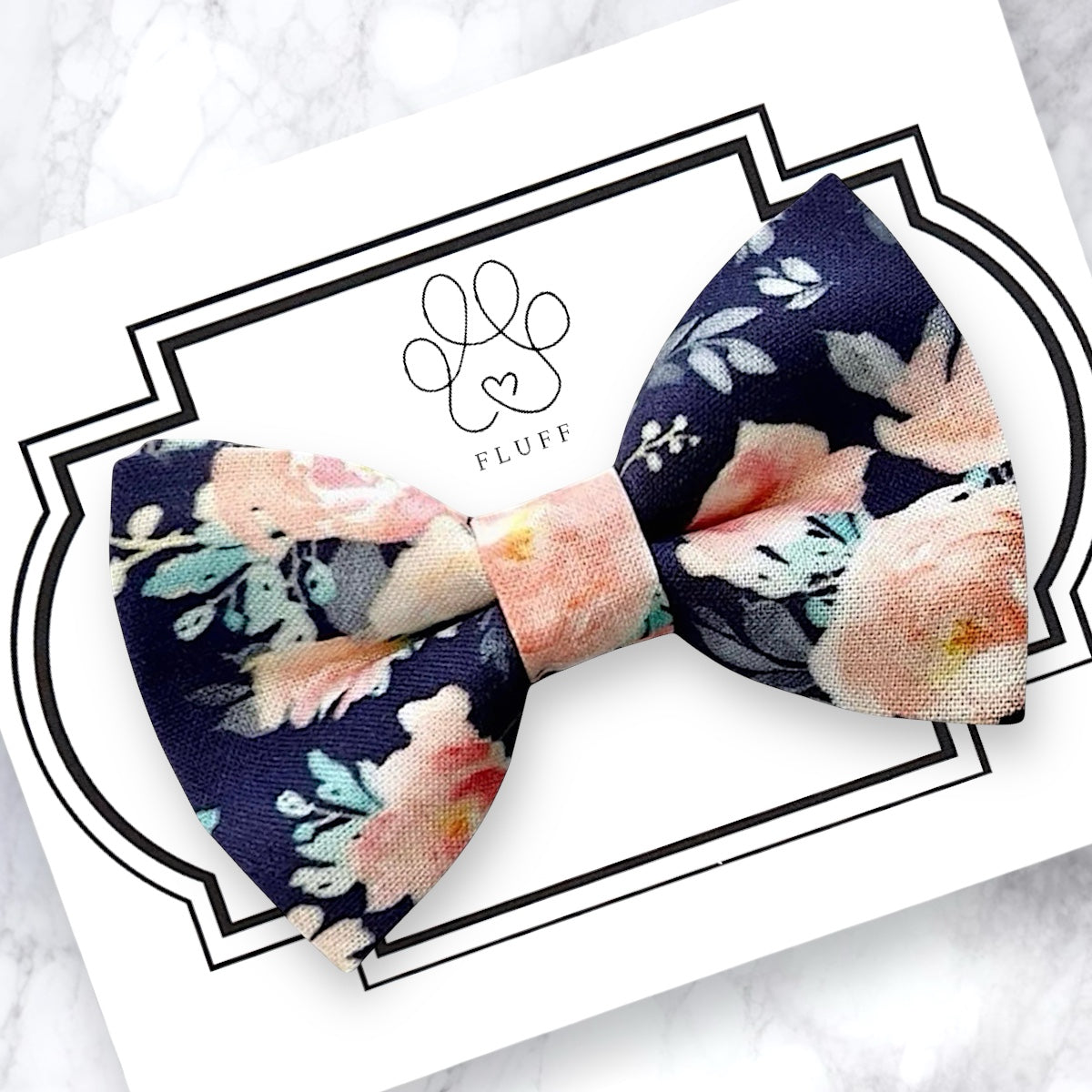 Floral dog bow tie with pink flowers on a navy blue background on a card with 'FLUFF' branding
