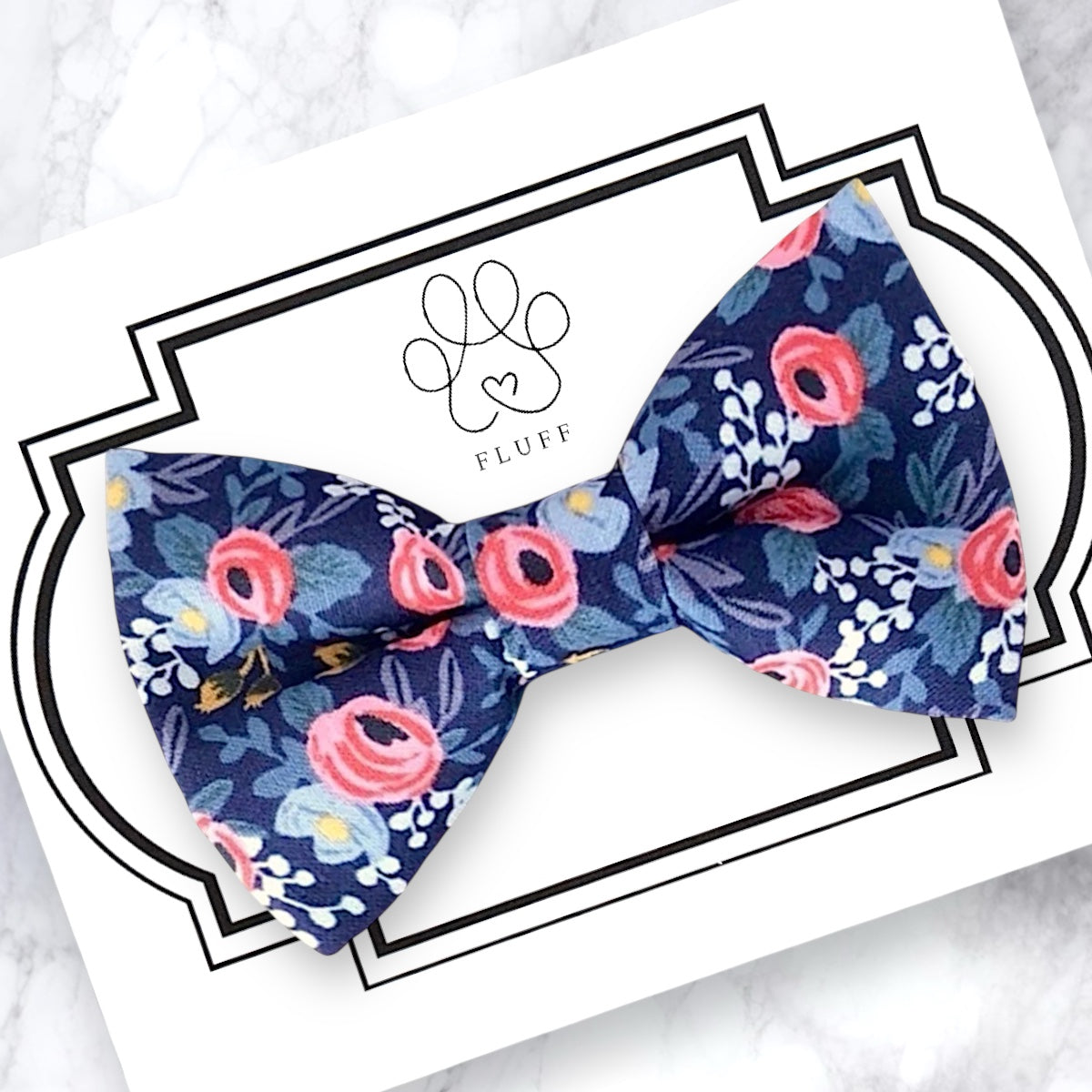 Navy blue and pink floral patterned bow tie on a branded card with a white background