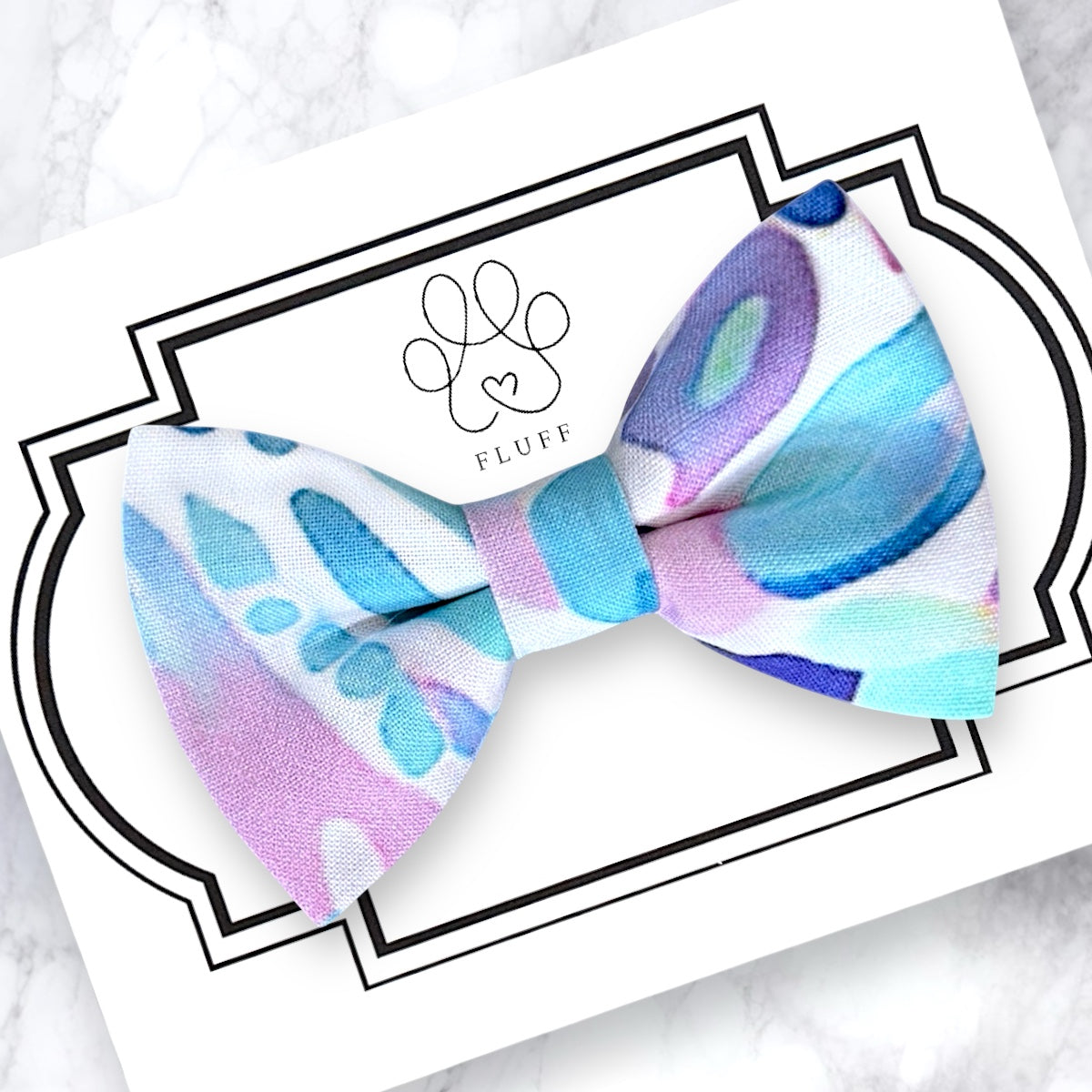 Colorful abstract-patterned dog bow tie on a white card with 'FLUFF' branding.
