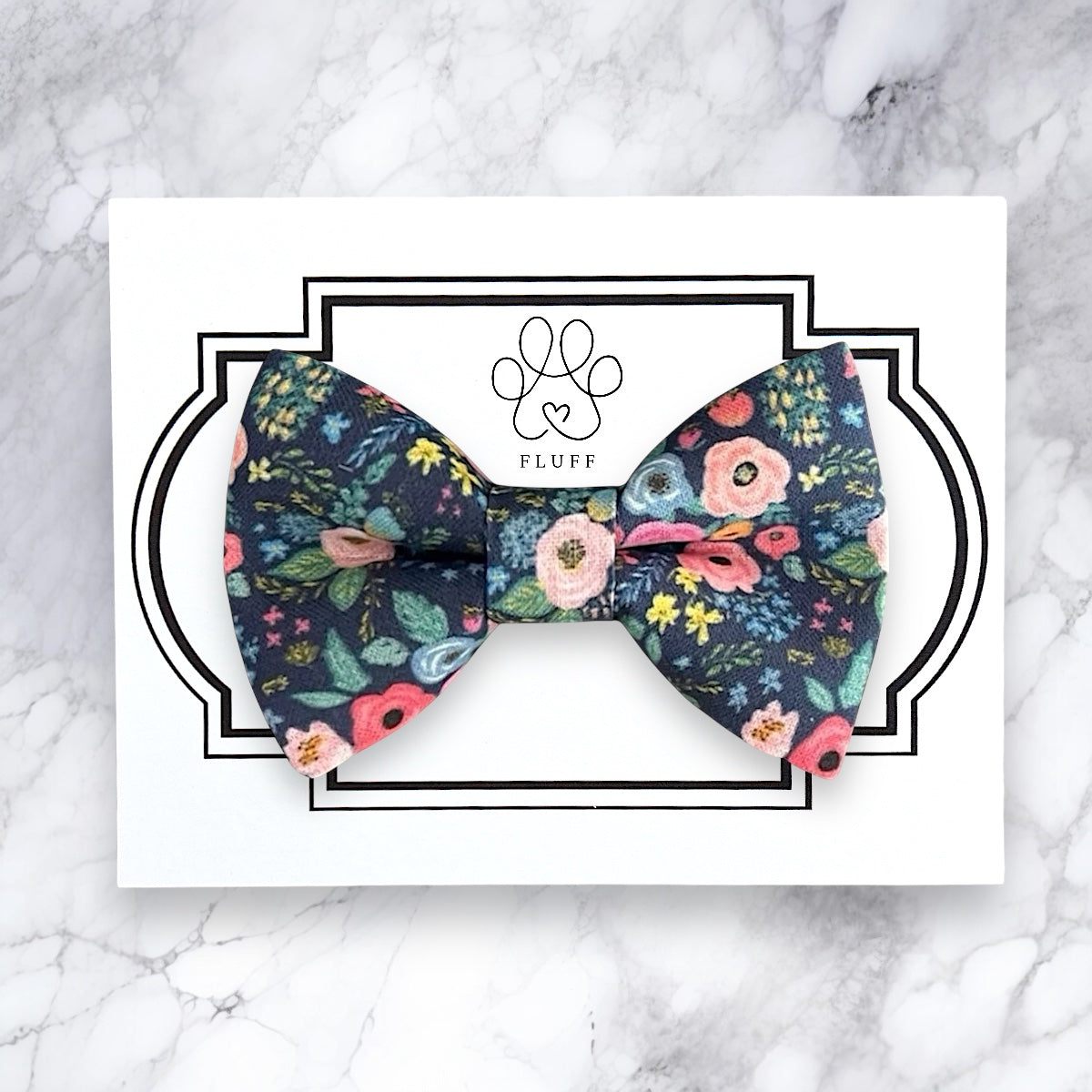 Navy floral bow tie on a white card with 'FLUFF' branding on a marble background
