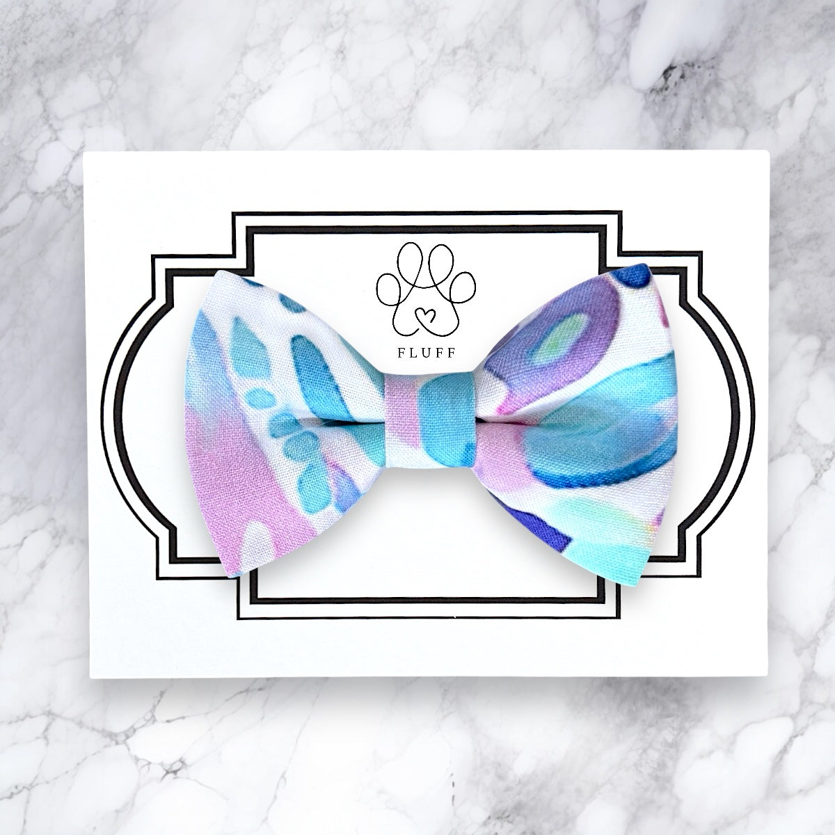 Colorful dog bow tie with 'FLUFF' branding on a marble background