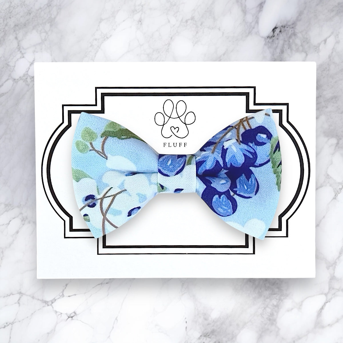 Floral dog bow tie with 'FLUFF' branding on a marble background