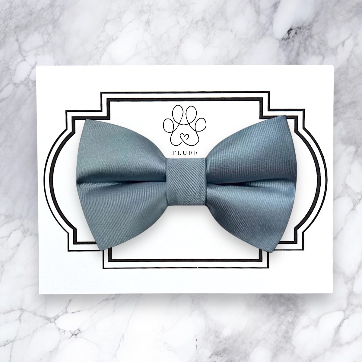 Dusty blue satin dog bow tie on a white card with 'FLUFF' branding on a marble background