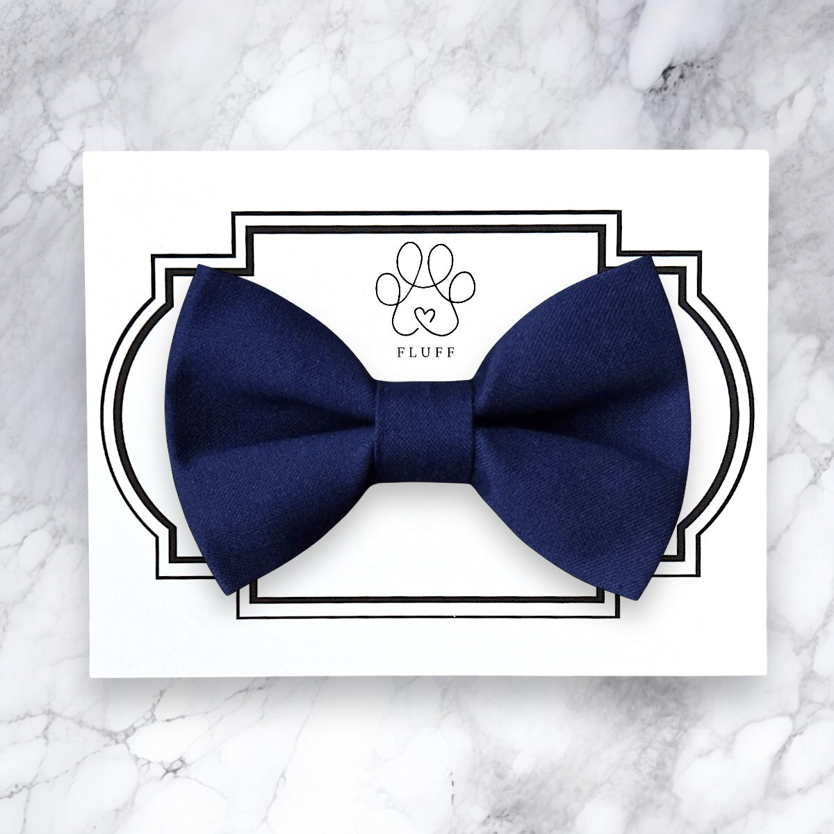 Navy blue dog bow tie on a white card with 'FLUFF' branding on a marble background