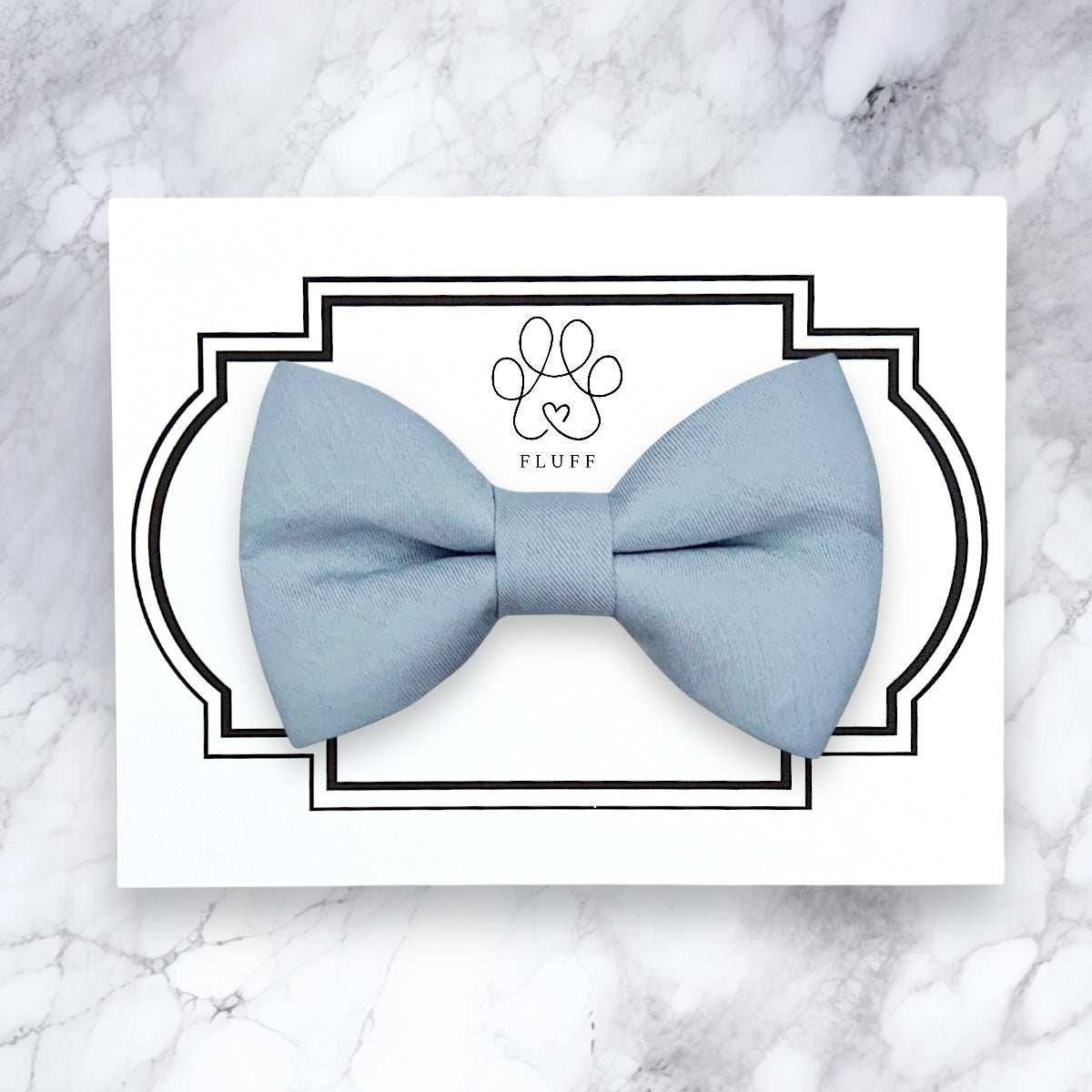 Light blue bow tie on a white card with 'FLUFF' branding on a marble background