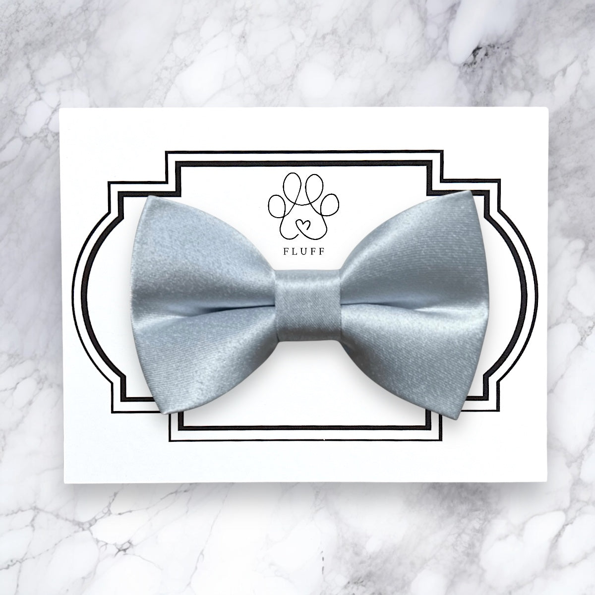 Blue dog bow tie on a white card with 'FLUFF' branding on a marble background