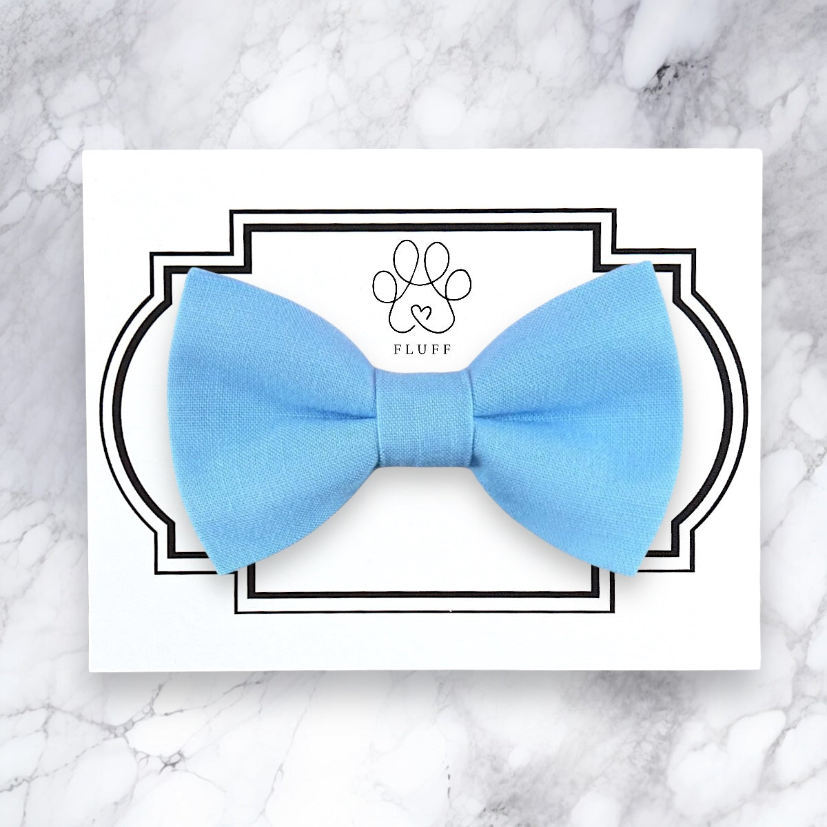 Light blue dog bow tie on a white card with 'Fluff' branding on a marble background