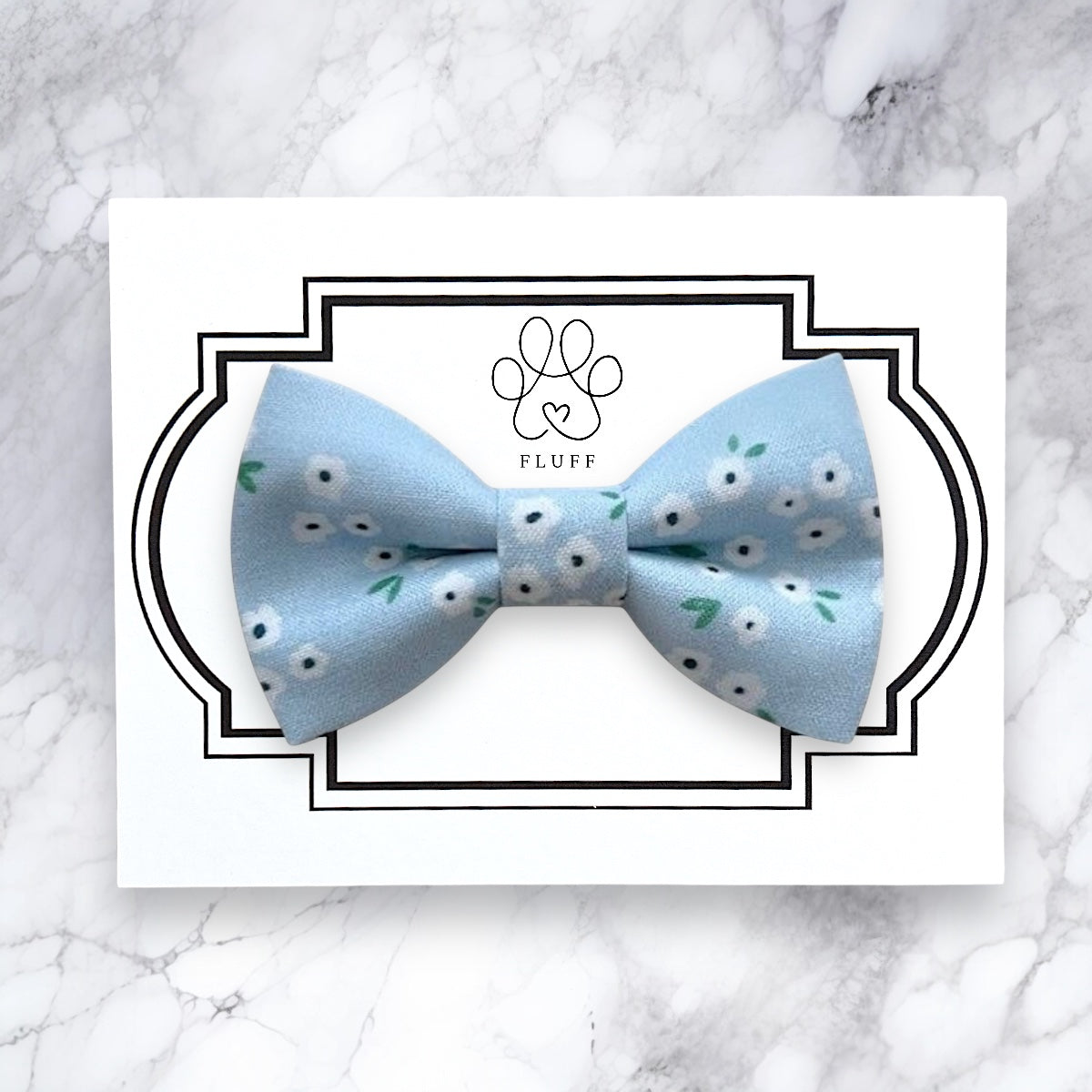 Light blue dog bow tie with white floral pattern on a marble background