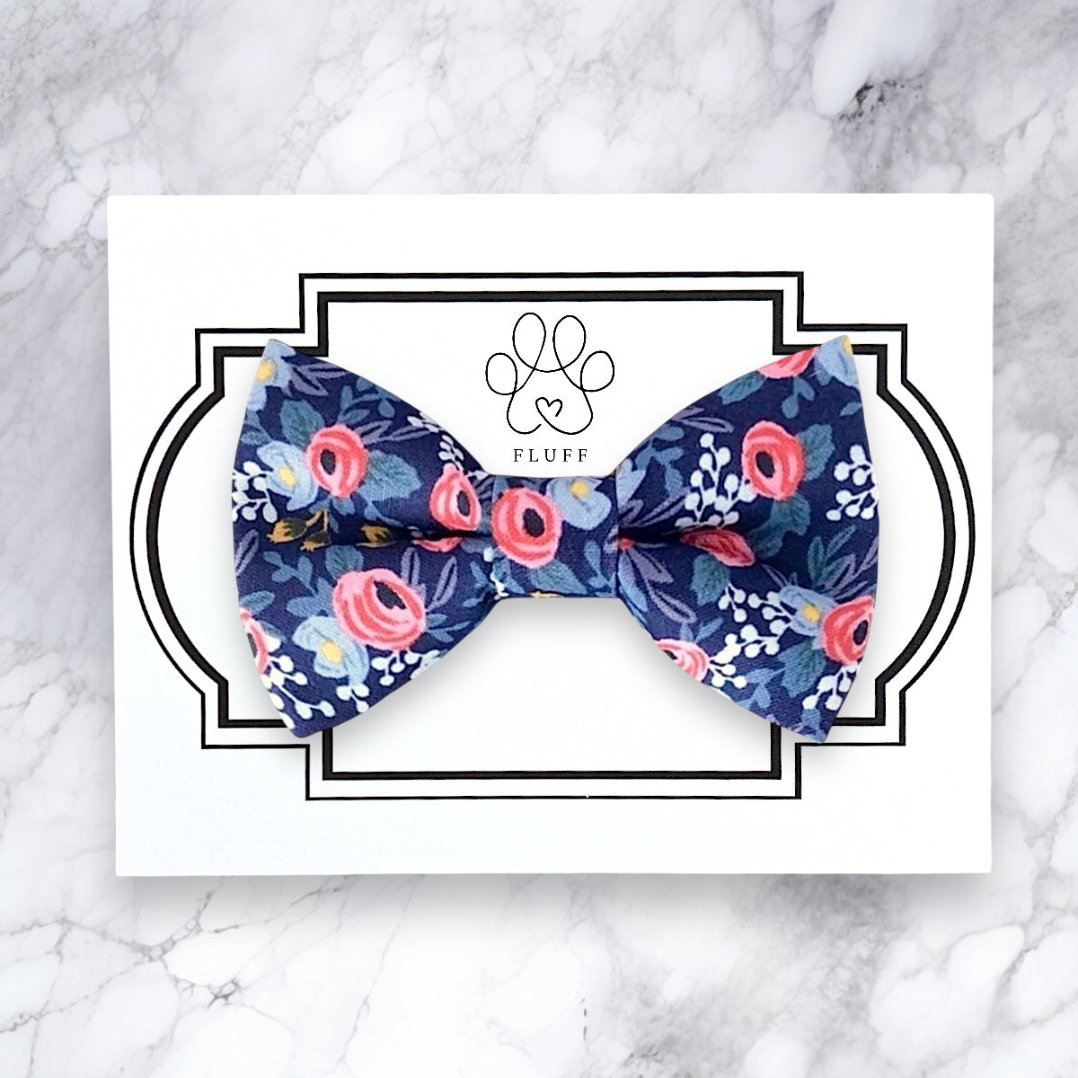 Floral patterned dog bow tie on a white card with 'FLUFF' branding on a marble background