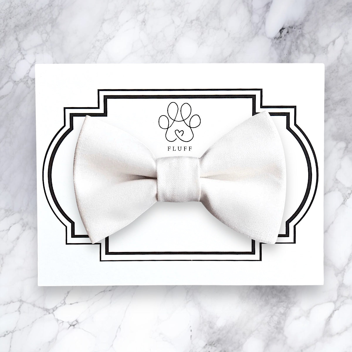 White dog bow tie on a card with 'FLUFF' branding on a marble background