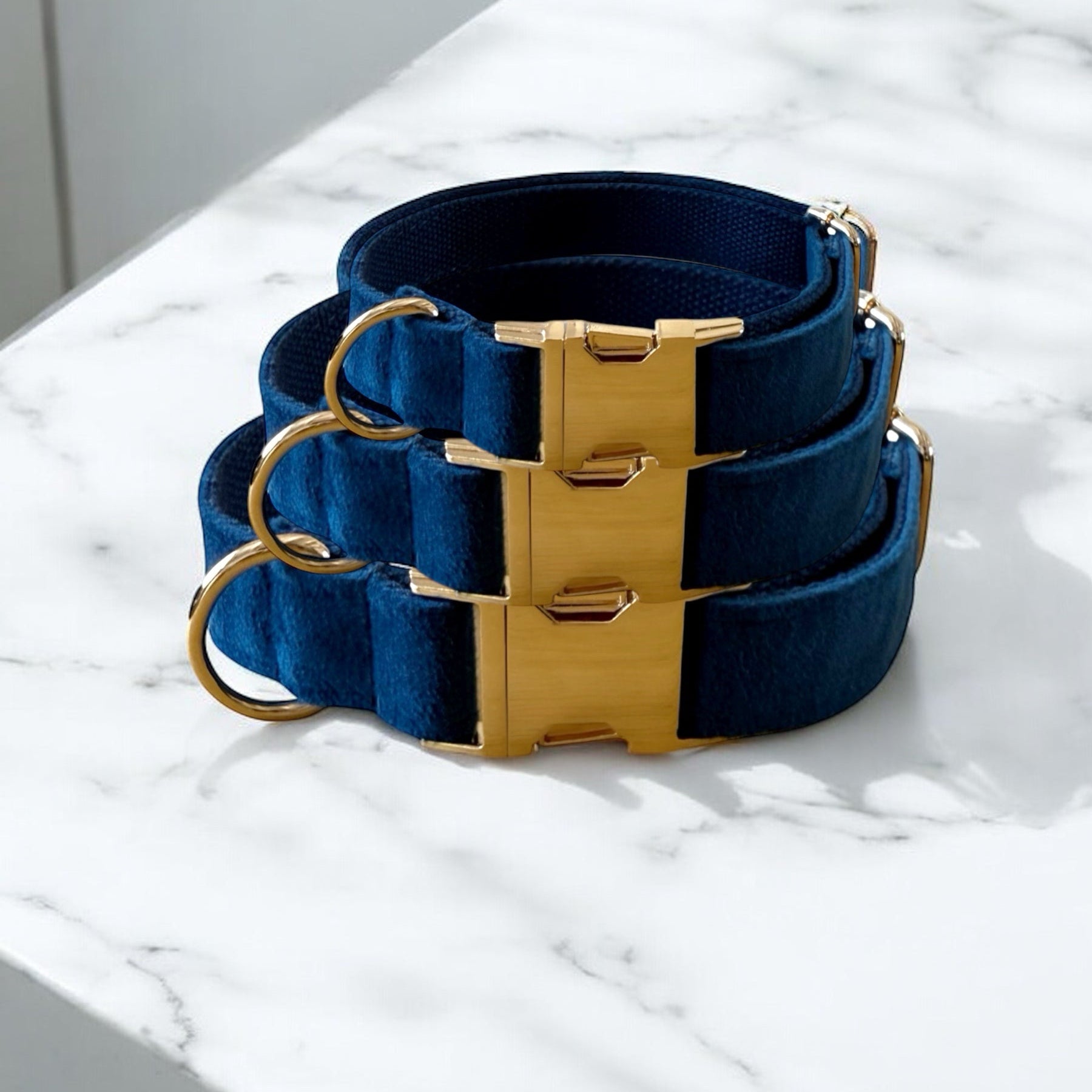 Set of blue dog collars with gold buckles on a marble surface