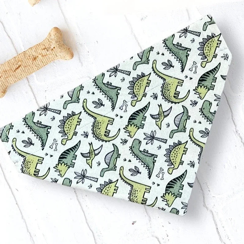 a dog bandana with dinosaurs on it next to a bone