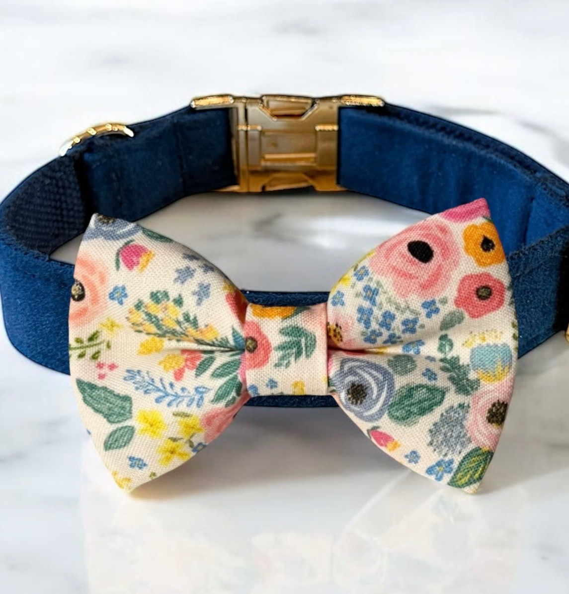 A blue collar with a gold buckle and a colorful bow tie with a floral pattern.