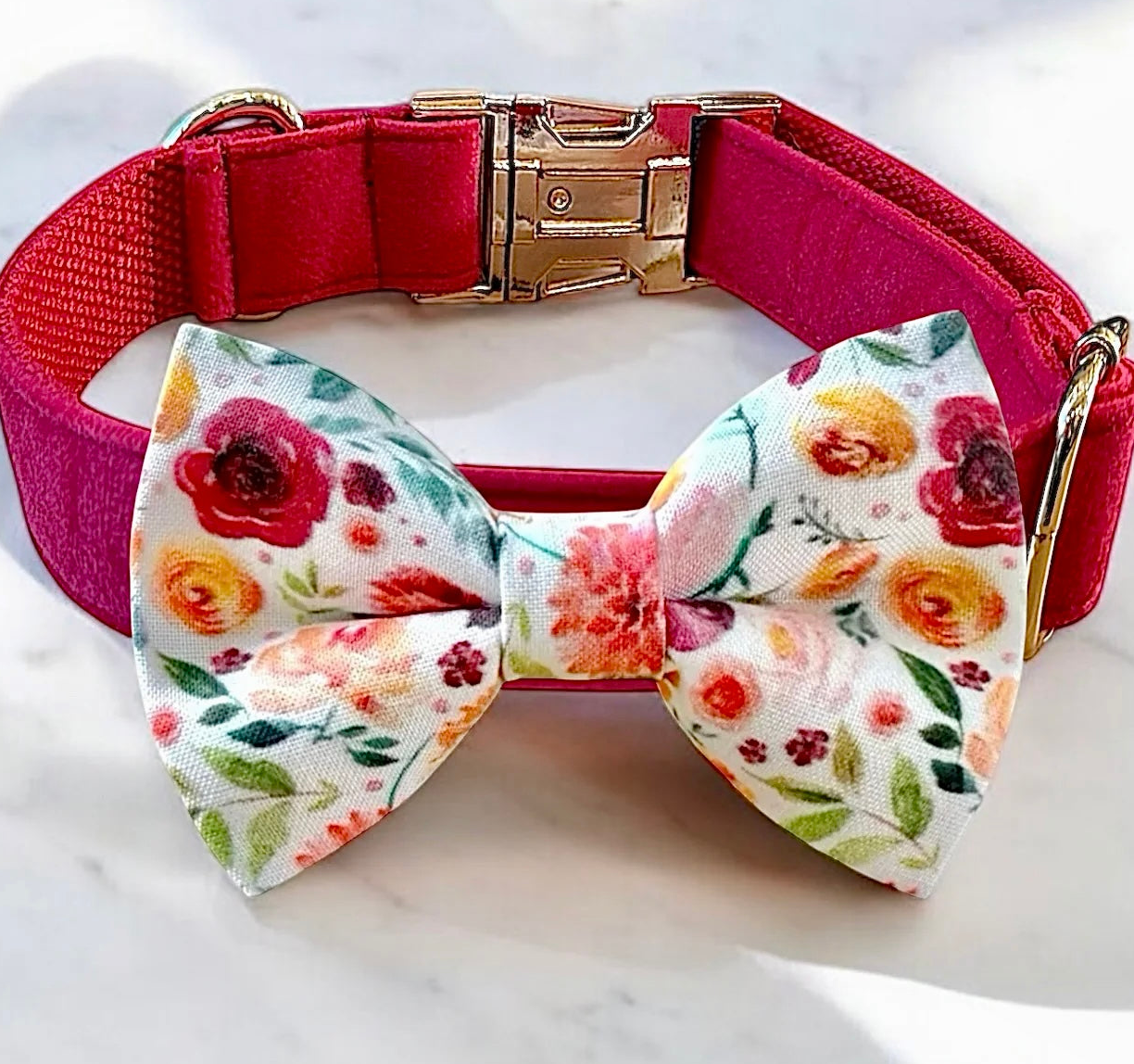 A pink collar with a floral print bow tie is displayed on a white marble surface.