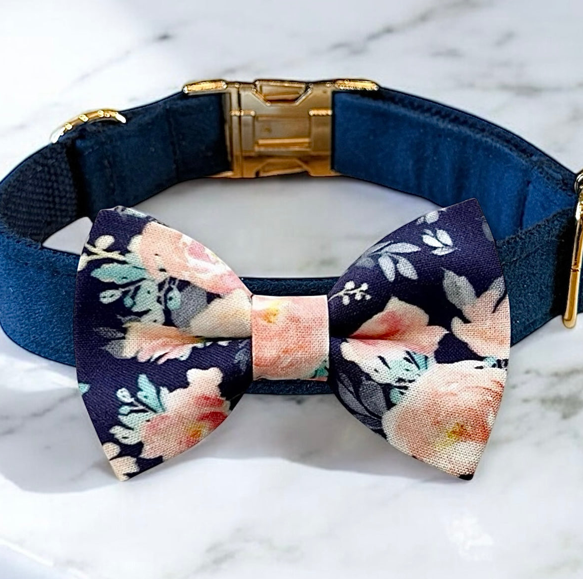 A navy blue dog collar with a gold buckle and a bow tie with a floral pattern.