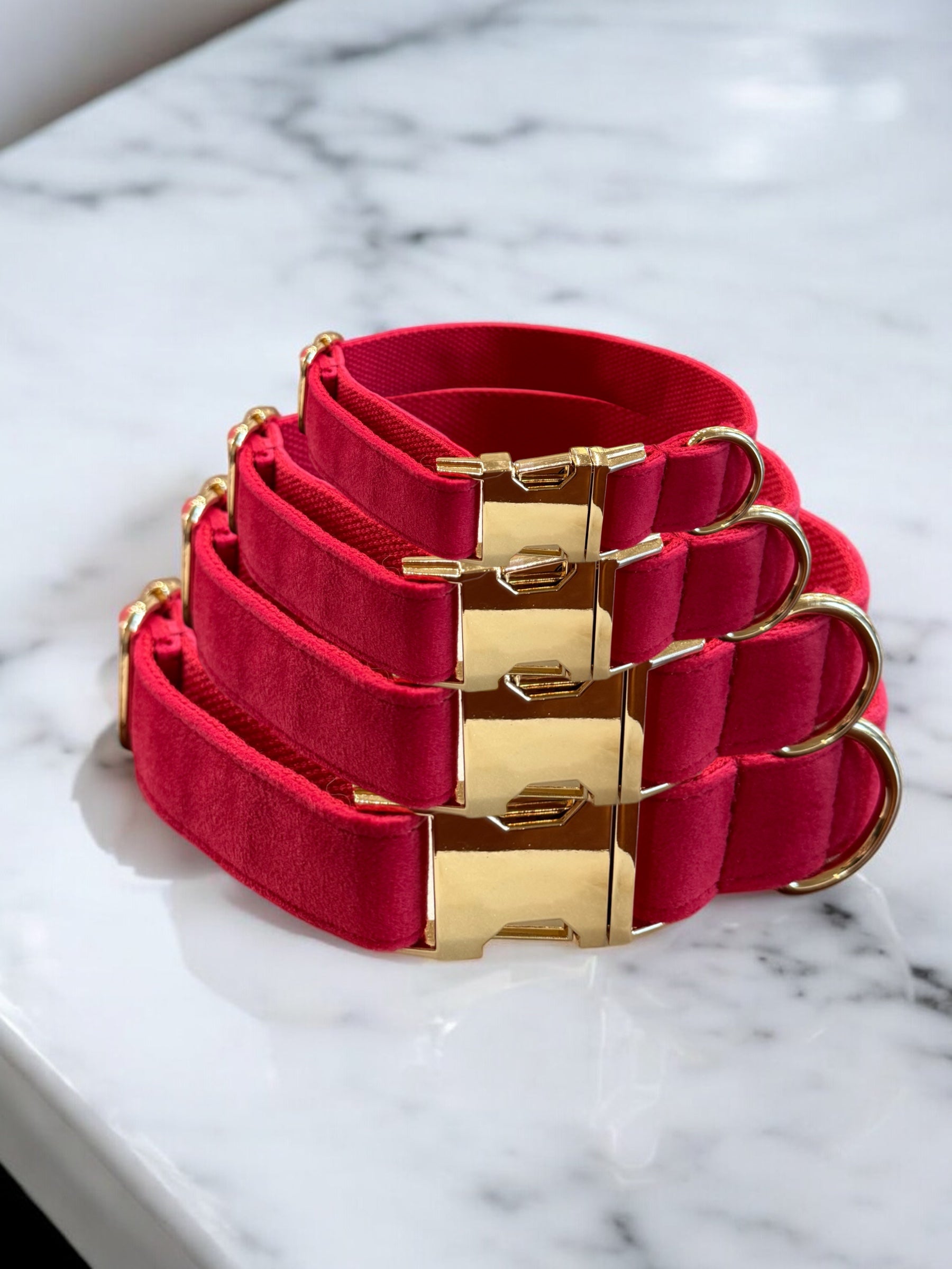 Set of pink dog collars with gold buckles on a marble surface