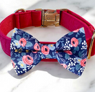 A pink collar with a gold buckle and a blue bow tie with a floral pattern are displayed on a white marble surface.