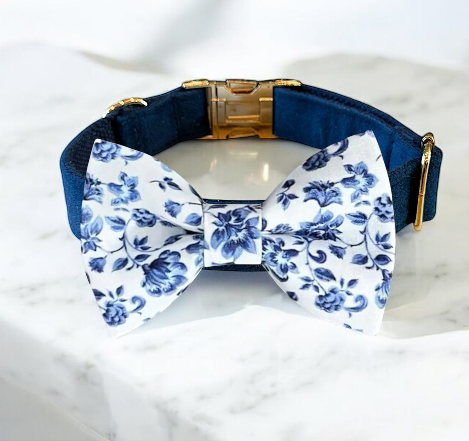 Navy dog collar with a white floral bow tie on a marble surface