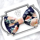 Floral dog bow tie with pink flowers on a navy blue background on a card with 'FLUFF' branding