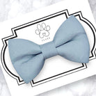 Dusty blue bow tie on a white card with a decorative border and brand logo.