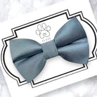 Dusty Blue dog bow tie on a white card with a brand logo, on a marble surface.